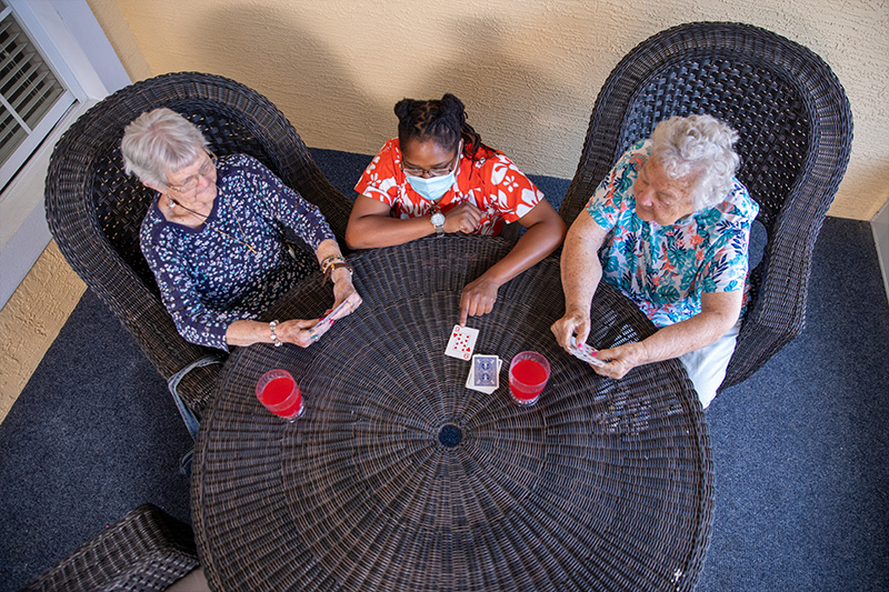 two senior care residents and care provider participating in a card game